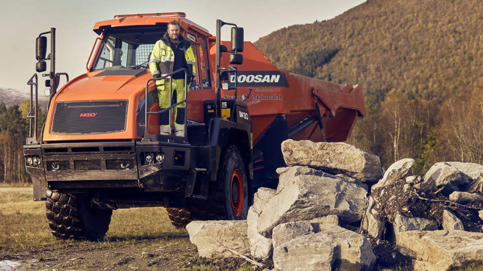 Sivert Malmedal står på sin oransje Moxy-dumper fra Doosan, med romsdalsfjell i bakgrunnen