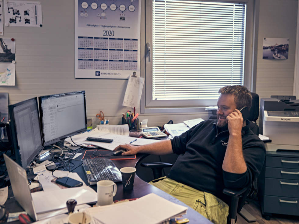 Sivert sitter på kontoret og svarer en kunde på telefon, med regnskapssystemet oppe på skjermene foran seg